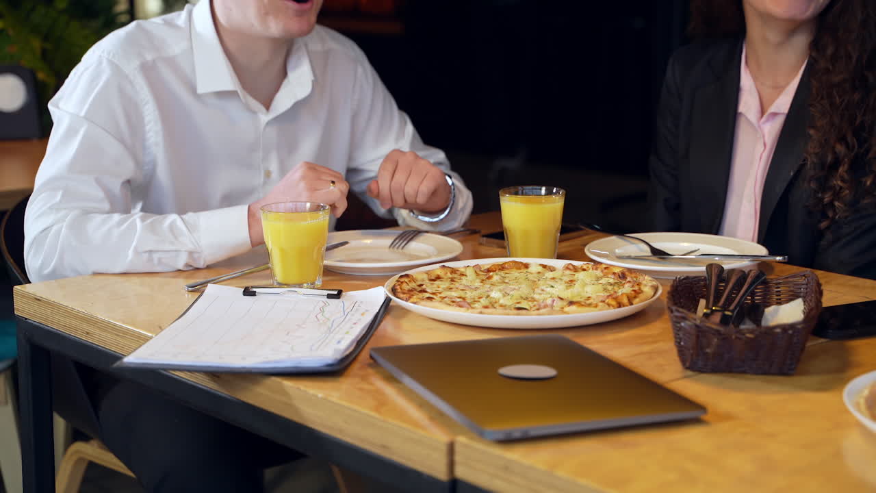 Office colleagues came to have business lunch at café. People wearing official clothes sit at the table with pizza and juice.