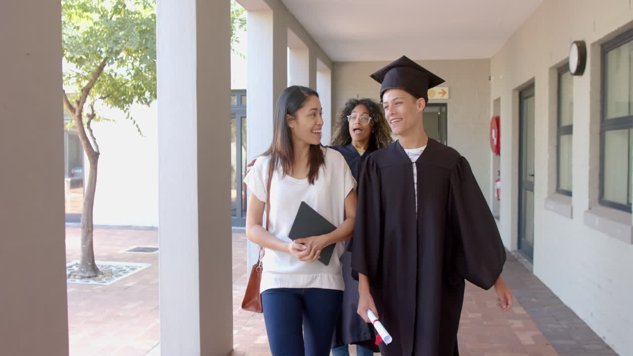 un adolescente biracial en traje de graduación camina con dos mujeres en la escuela secundaria