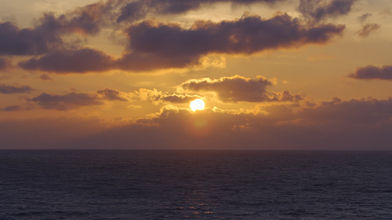 Solnedgang over havet i Estland, med solstråler, der strømmer gennem skyerne, roligt vand nedenfor
