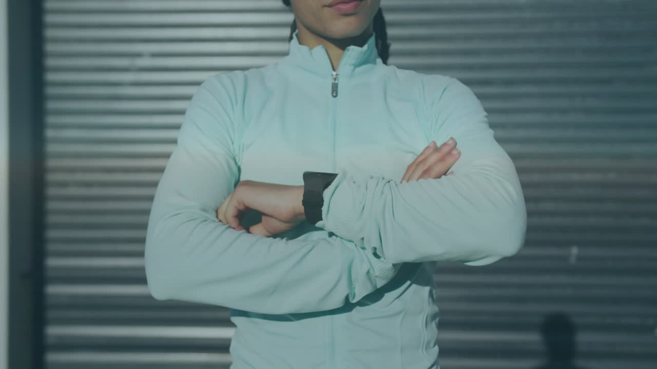 Woman standing arms crossed narrowing gaze, wrist device activating fitness HUD showing metrics