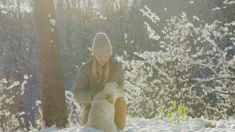 a young woman petting her dog while walking together in a picturesque winter park