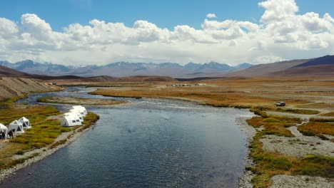 drones aéreos volando entre lujosas tiendas de campaña a lo largo de un río natural vacío en la llanura alpina de gran altitud del parque nacional deosai ubicado entre skardu y el valle de astore en pakistán mientras está soleado