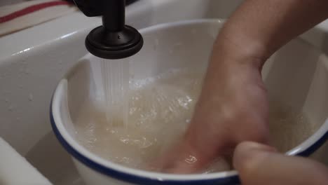 el chef lava el arroz dentro de un plato hondo bajo el agua en el fregadero