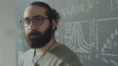 portrait of a bearded man with glasses in a classroom with a chalkboard