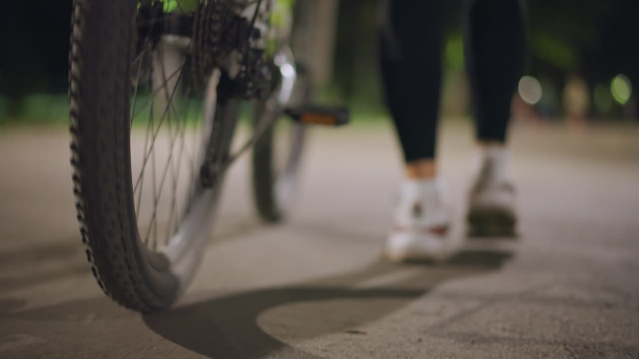 Pedestrian Rides Smoothly, Evening Streets Glow With Shadows, Nighttime Cityscape With Moving Figures And Lights, Person Walks Alongside Bike Under Glowing Streetlights Creating Deep Shadows