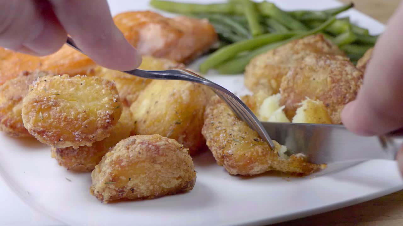 Slow Motion Slider Shot of Cutting into a Roast Potato on a White Plate With Green Beans and Salmon