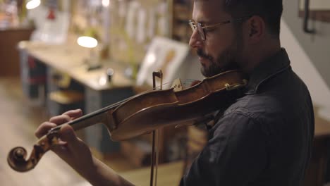 un luthier barbudo adulto tocando un violín hecho a mano