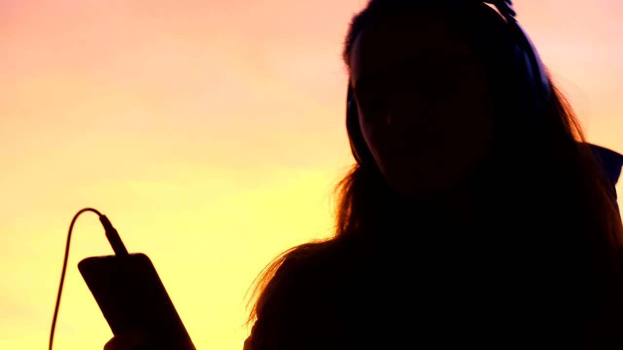 夕暮れの街で電話で音楽を聴いて踊っている女性のシルエット