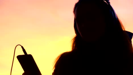 silhouette of woman dancing and listening to music on phone in city at sunset