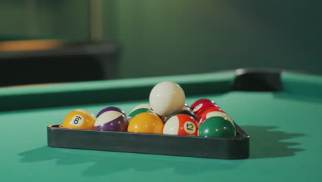 close-up view of colorful billiard balls neatly arranged in triangle rack on green pool table, with vibrant colors and soft lighting highlighting their texture and smooth surface in a cozy game room