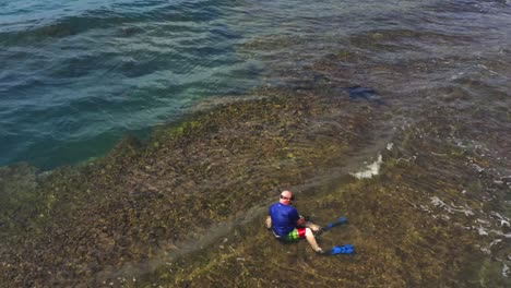 Scuba-diver-wearing-flippers,-sitting-on-Panama-coral-reef-coastline-preparing-to-explore-blue-water-seascape