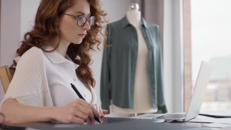 Ginger-adult-woman-using-laptop-and-digital-tablet-at-work.