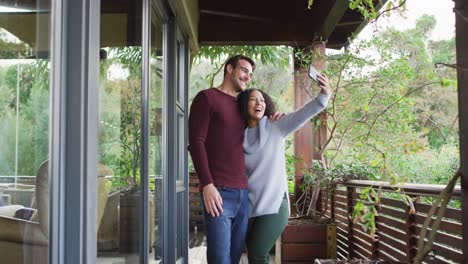 casal de raça mista sorrindo enquanto tira uma selfie no smartphone na varanda da casa de férias