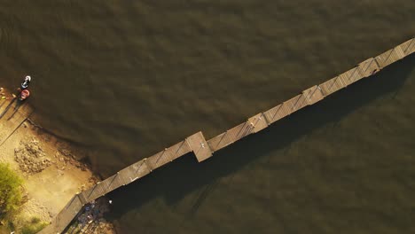 Aerial-top-down-circling-over-two-people-walking-on-pier-at-sunset,-Fray-Bentos-in-Uruguay