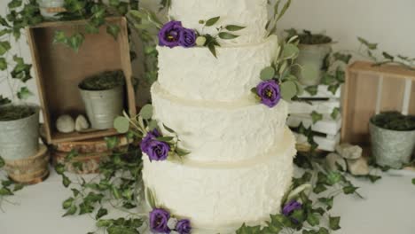 Gorgeous-panning-shot-of-a-white-tiered-wedding-cake-with-a-beautiful-floral,-wood-and-candle-décor-backdrop-at-Le-Belvédère-in-Wakefield,-Quebec,-Canada