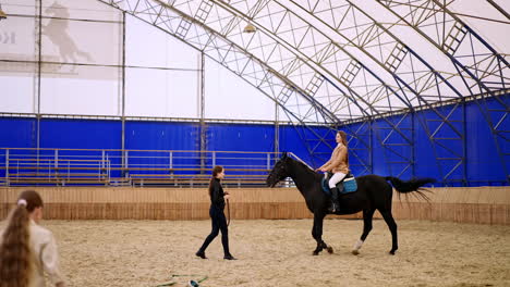 long-haired woman riding a beautiful black horse. female lady coach walks in front of animal. young girl comes up to the foreground.