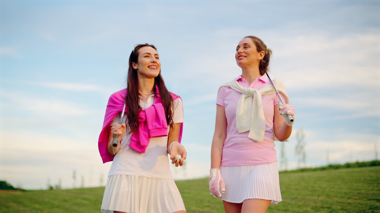 Zwei Frauen in weißer und rosafarbener Kleidung spielen mit einem weißen Golfball auf dem Platz