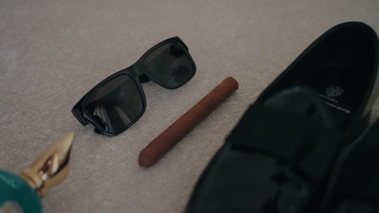 flatlay of groom essentials with black shoes sunglasses cigar and car key