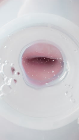 child mouth drinks clear water from baby measuring bottle. lips hold nipple and bubbling water sways in transparent container macro low angle shot