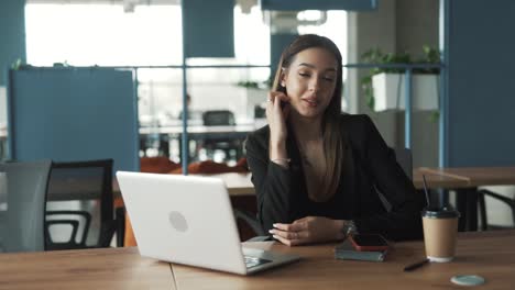 Retrato-Detallado-De-Una-Hermosa-Joven-En-Una-Elegante-Oficina-De-Coworking-Mirando-A-La-Cámara-Y-Sonriendo,-Vestida-Con-Un-Traje-De-Negocios-Clásico