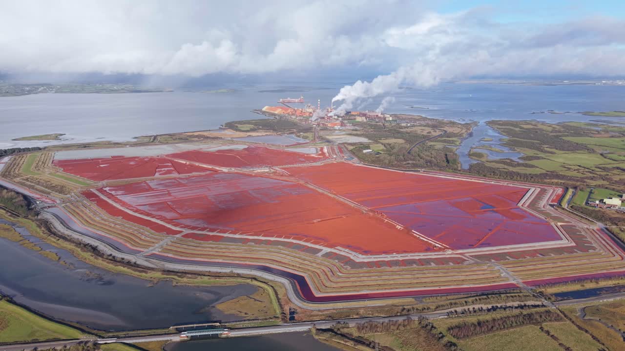 Reddish Mud Waste Pool Of Aughinish Alumina Refinery In County Limerick, Ireland. aerial pullback shot
