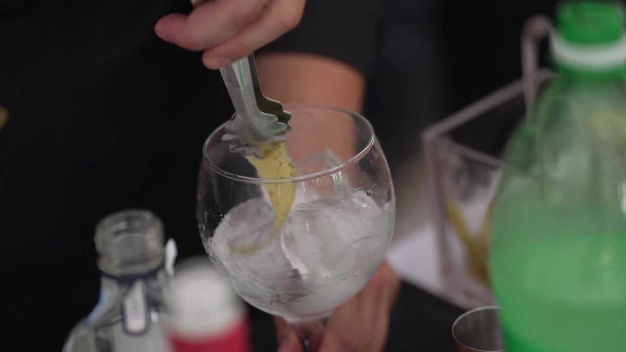 Nærbillede af tilberedning af en cocktail med pynt og is i et glas på en bar