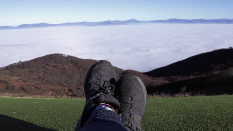 toma de zapatos deportivos de una persona descansando en la cima de una montaña mientras mira hacia el horizonte