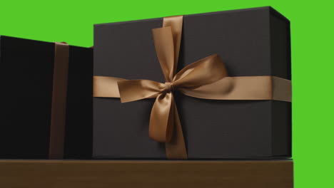 Close-Up-Of-Gift-Wrapped-Presents-Decorated-With-Ribbon-On-Table-Shot-Against-Green-Screen