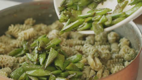 cook adding green beans to pasta in pan