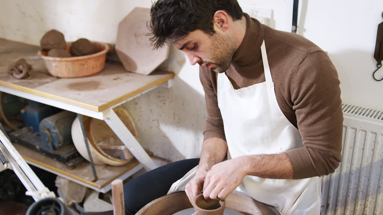 Joven con delantal trabajando en el torno en un estudio de cerámica.