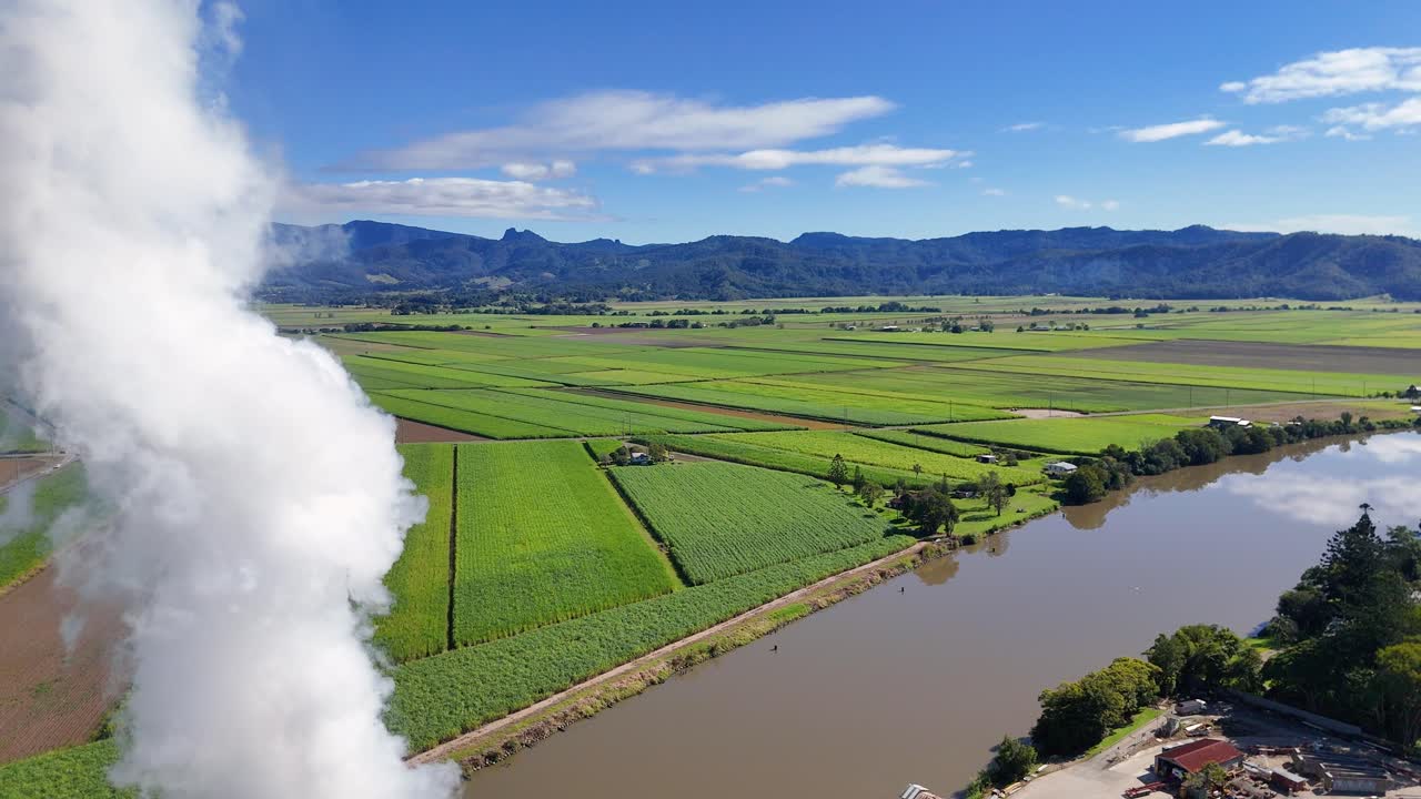 Aerial footage of sugar cane fields and a river with steam rising, under clear blue skies in Gold Coast, Australia