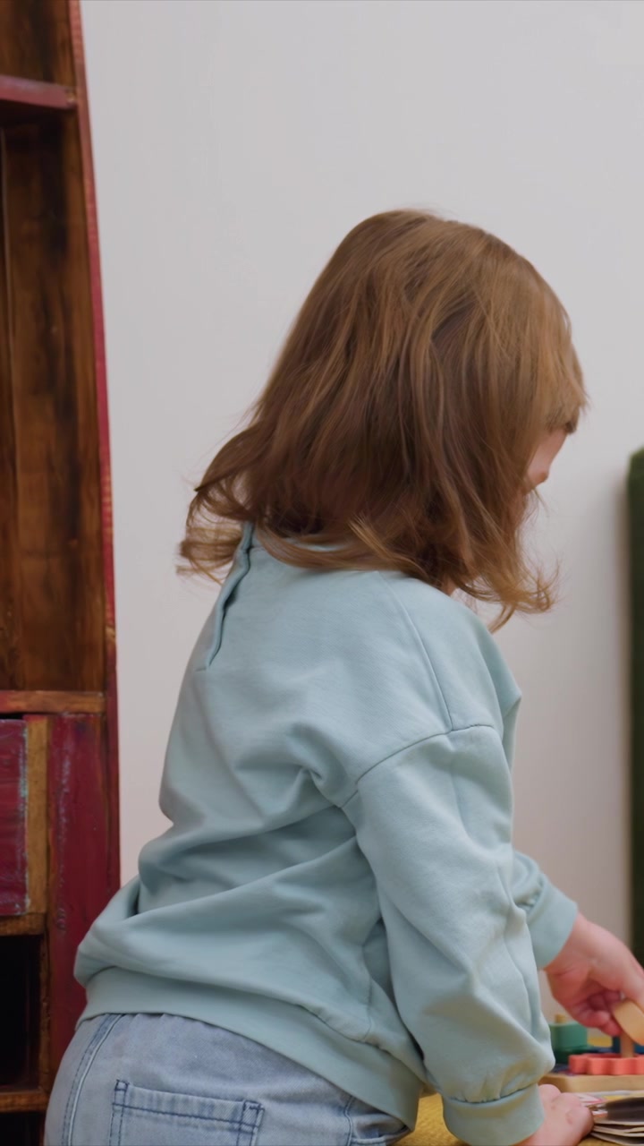 Persona concentrata durante un'attività che coinvolge forme geometriche. La mano sinistra si protende verso blocchi colorati disposti. Pareti bianche fanno da sfondo mentre una ragazza si impegna a un ritmo costante.