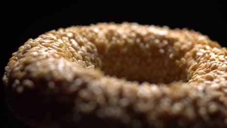 fresh bagels with sesame seeds in rotation. black background. extreme closeup.