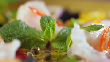 extreme close-up of a ceviche dish, with the chef placing mint leaves on it, it has capers, white fish, hot pepper, tomatoes and olive oil - a colorful and healthy spanish-american dish