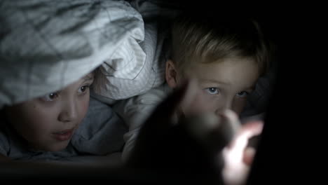 two boys lying in bed at night watching movie on pad