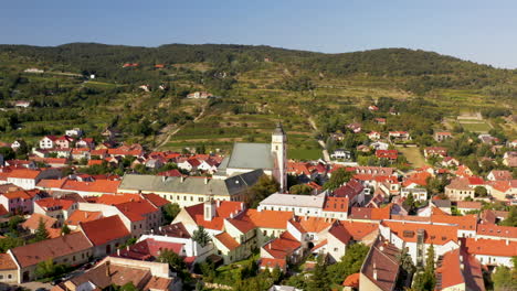 drone shot of the church of holy trinity in svätý jur or saint george in bratislava, with a flock of birds flying past the camera