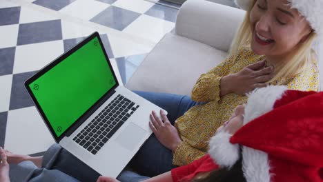 Mutter-Und-Tochter-Mit-Weihnachtsmütze-Unterhalten-Sich-Zu-Hause-Auf-Dem-Laptop-Per-Video