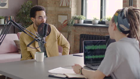 man talking into a microphone with woman sitting at desk with laptop with equalizer on the screen