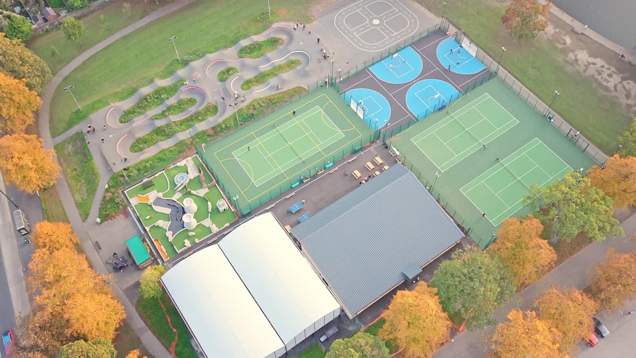 Top-down aerial reveals Hillsborough Park’s full suite of sports facilities, three green tennis courts, basketball courts, grey multi-use court, playground, and winding BMX pump track in Sheffield