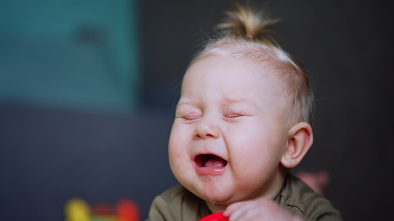 Lovely blue-eyed blond baby chewing a red toy. Close up portrait of an infant of six months old.