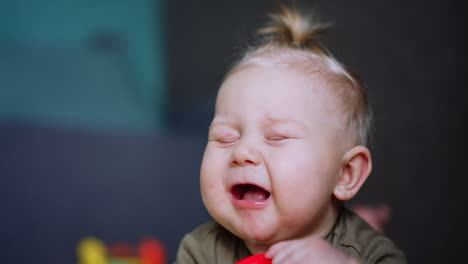 lovely blue-eyed blond baby chewing a red toy. close up portrait of an infant of six months old.