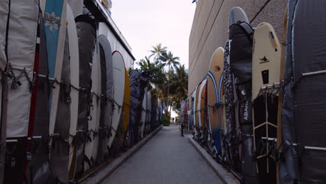 Rows-of-Colorful-Surfboards-Standing-Vertically-Along-Narrow-Passageway-to-Beach,-Waikiki,-Wide