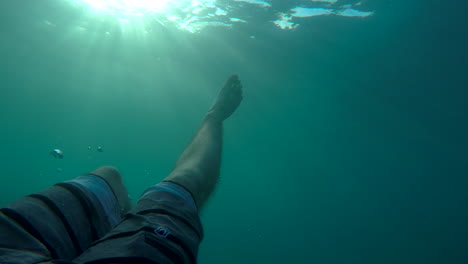 slow motion pov underwater shot showing shorts and legs, as a man floating upside down under the surface of the ocean