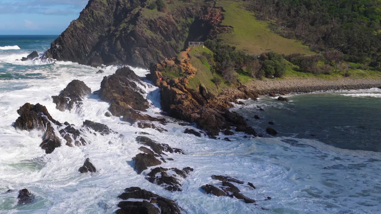 Dynamic aerial view of waves crashing against rocky shoreline at Byron Bay, showcasing vibrant ocean hues and rugged coastal landscape