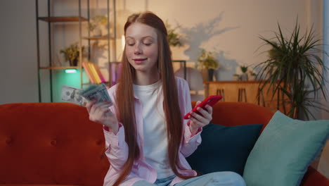 smiling happy young teen child girl counting money cash use smartphone, income, saves, lottery win