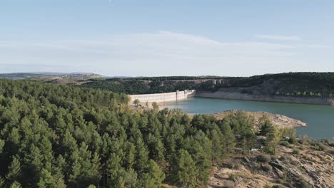 Vista-Aérea-De-Una-Presa-Hidroeléctrica-Rodeada-Por-Un-Embalse-Y-Pinos-En-La-Orilla