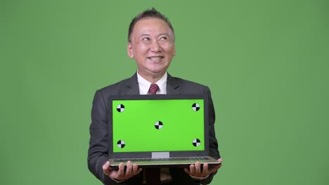 成熟した日本人のビジネスマンがラップトップを展示している