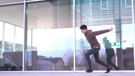 una toma en cámara lenta de un joven freerunner haciendo trampa frente a una pared de vidrio