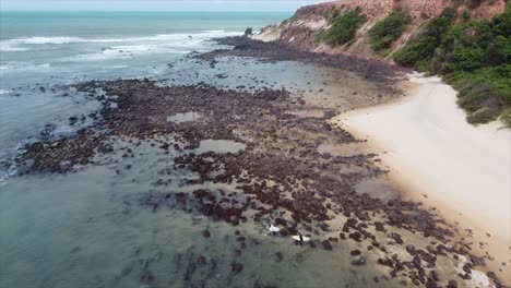 toma panorámica de surfistas caminando hacia el océano en la playa tropical de brasil playa de pipa, brasil por drone 4k