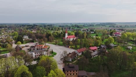 drone pulls back from rucava lutheran church surrounded by green trees, latvia